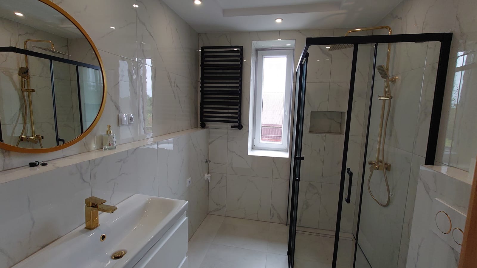 Nowoczesna łazienka z kabiną prysznicową typu walk-in, marmurowe płytki, złota armatura i okrągłe lustro z podświetleniem LED. Minimalistyczny design.