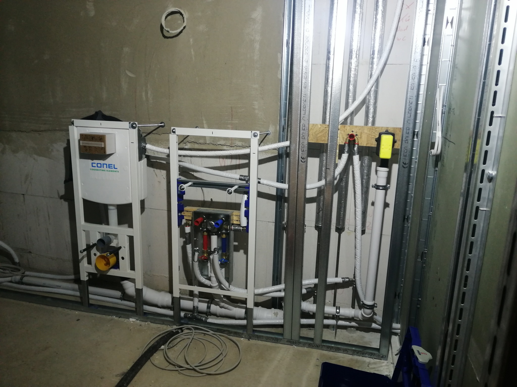 Instalacja podtynkowa WC w trakcie montażu: biała rama, rury w izolacji, metalowy stelaż. Widoczne elementy mocujące i przyłącza. Surowy stan wykończenia wnętrza.