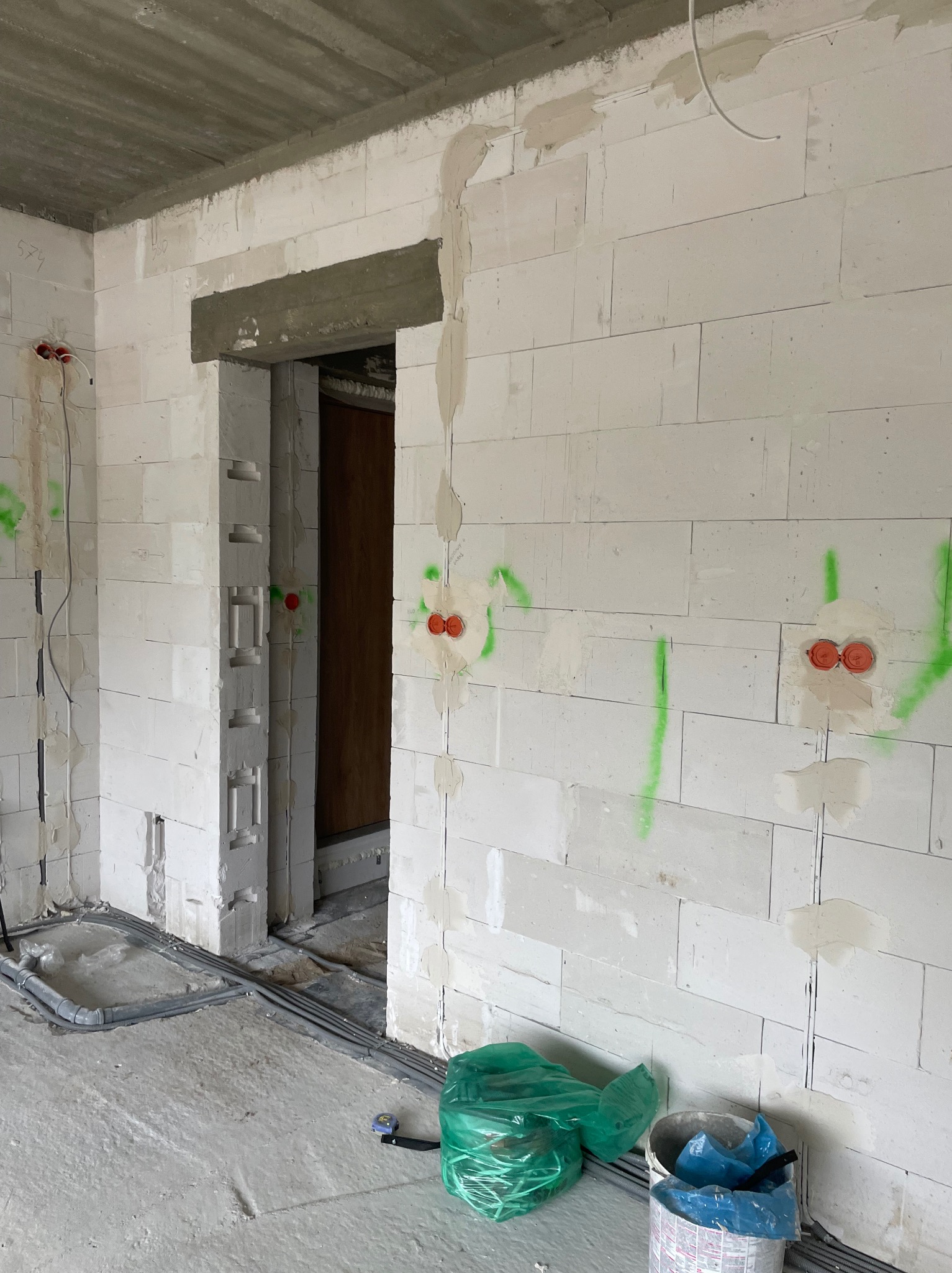 Wnętrze w trakcie prac instalacyjnych: ściany z betonu komórkowego z wyznaczonymi punktami elektrycznymi, kable w podłodze, widoczny otwór drzwiowy.
