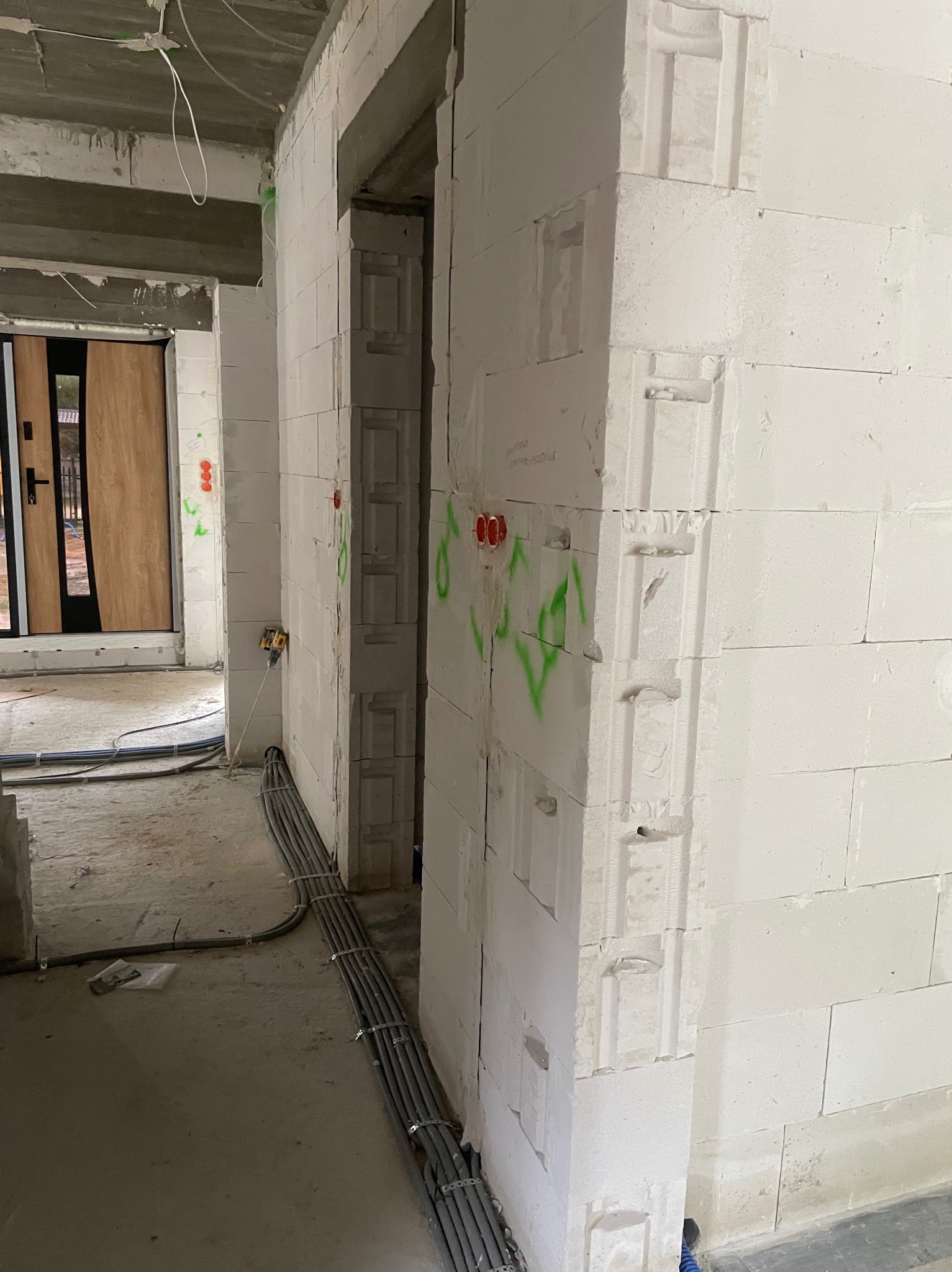 Surowy stan budynku z widocznymi przewodami elektrycznymi ułożonymi wzdłuż ściany z betonu komórkowego. Otwory na gniazdka zaznaczone zielonym sprayem.
