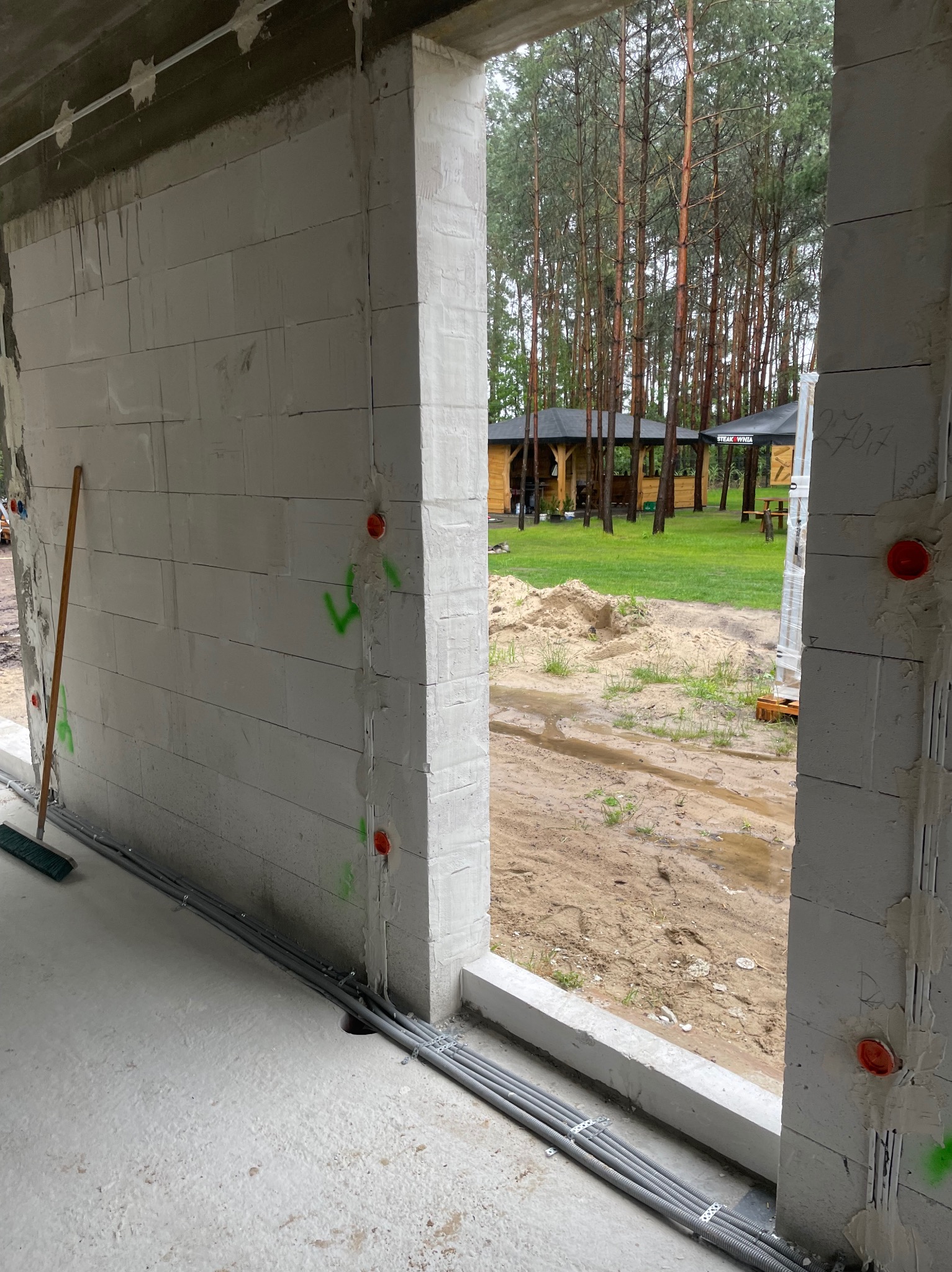 Surowy stan budynku z widoczną instalacją elektryczną w peszlach, prowadzoną wzdłuż ściany z betonu komórkowego. Na ścianie widoczne oznaczenia i puszki elektryczne.