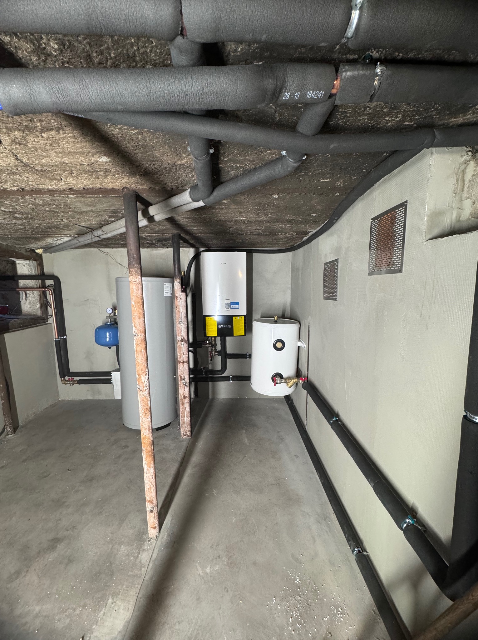 Zrealizowana instalacja CO w piwnicy: piec, zbiorniki, rury w izolacji termicznej. Widoczne zabezpieczenia, grzejniki i elementy instalacji.