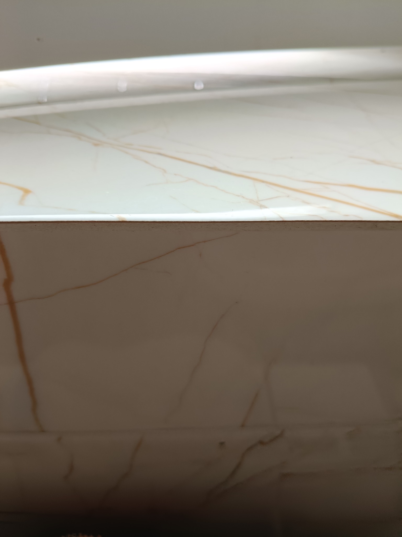 Detal marmurowej okładziny ściennej z subtelnym, złotym żyłkowaniem pod jasnym oświetleniem, ukazując precyzję wykonania i estetykę wykończenia.