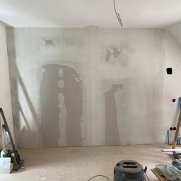 Wykończenia ,szpachlowanie ,malowanie ,płytki - Ściana po szpachlowaniu z widocznymi łatami, przygotowana do malowania. Na podłodze widoczny odkurzacz przemysłowy i narzędzia.