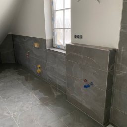 Wykończenia ,szpachlowanie ,malowanie ,płytki - Wykończona łazienka na poddaszu: szare płytki imitujące marmur na podłodze i ścianach, widoczne przyłącza wodno-kanalizacyjne, okno dachowe z białą ramą.