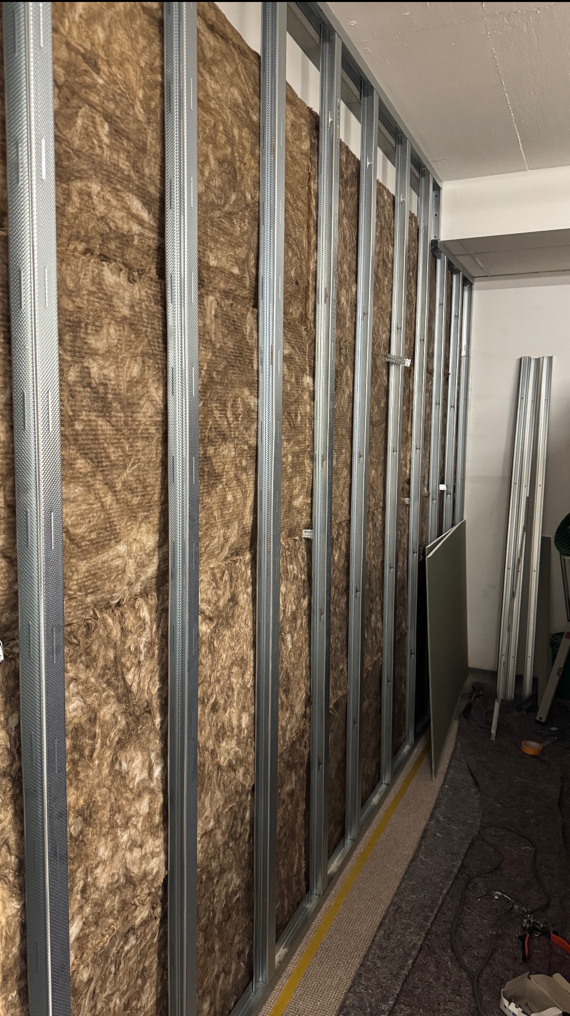 Montaż ścianki działowej z wełną mineralną i metalowym stelażem w Gniezno. Widoczne płyty karton-gips i narzędzia.