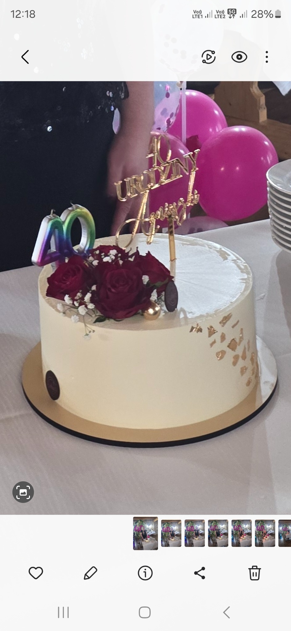 Tort urodzinowy z dekoracją z czerwonych róż, świeczką w kształcie liczby 40 i topperem '40 Urodziny Anny', różowe balony w tle.