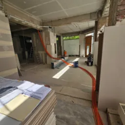 Instalacja elektryczna w trakcie remontu w Jelcz-Laskowice. Widoczne kable, płyty gipsowe i plany. Etap prac przed wykończeniem.