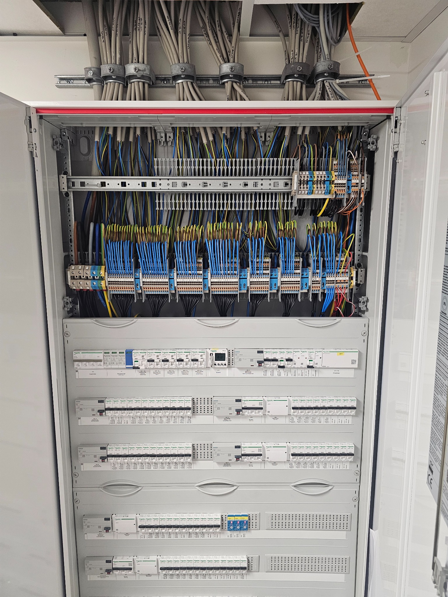 Rozdzielnica elektryczna z licznymi przewodami i zabezpieczeniami, widok z bliska na wnętrze szafy sterowniczej z zainstalowanymi elementami.