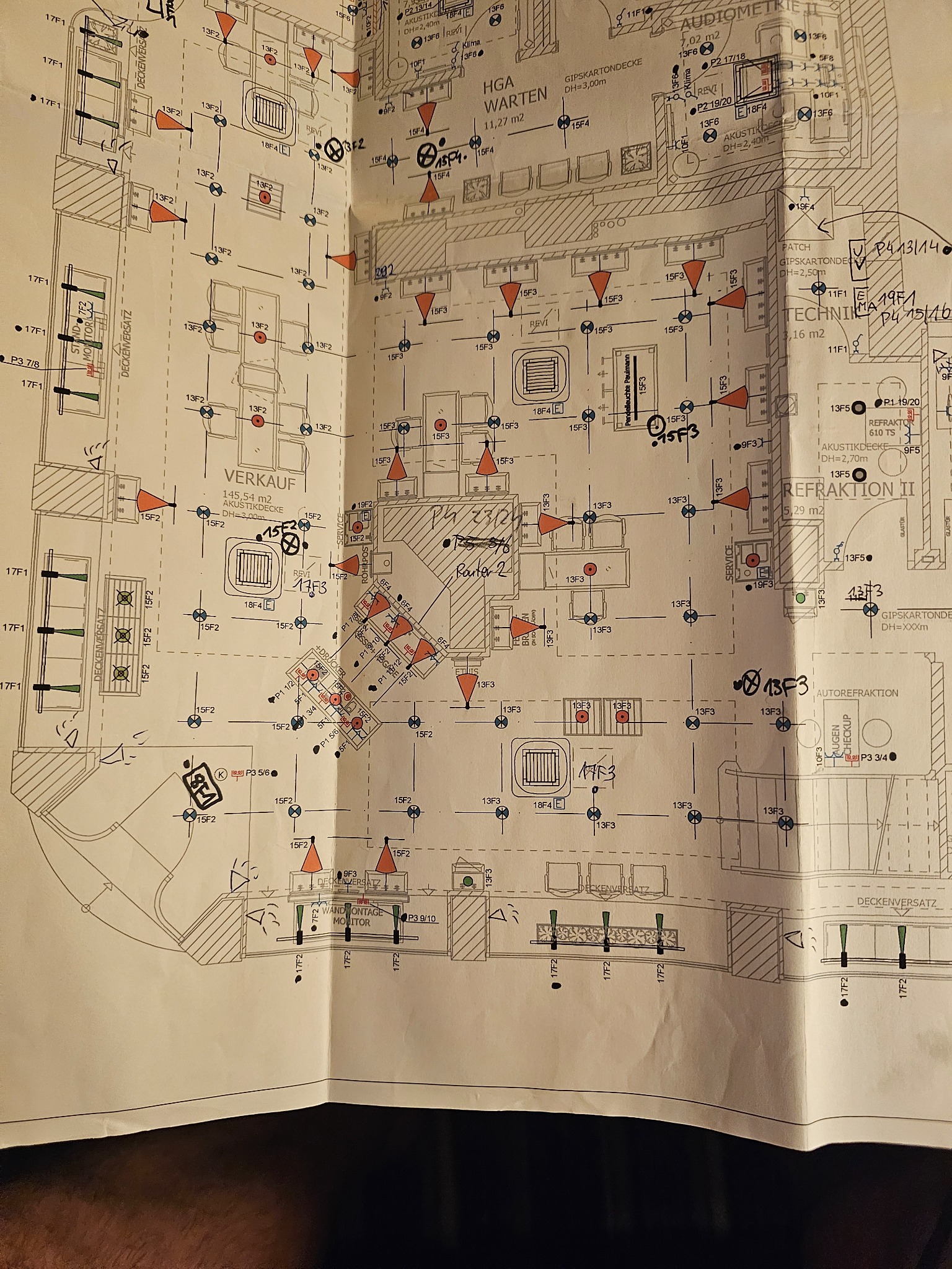 Szkic instalacji oświetleniowej na planie budynku, z naniesionymi oznaczeniami punktów świetlnych i tras kablowych. Widoczne odręczne notatki i pomiary.