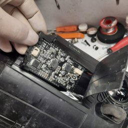 Kamil - Wymiana modułu DRL: ręka w rękawicy trzyma moduł elektroniczny w obudowie lampy samochodowej na warsztatowym stole z narzędziami.