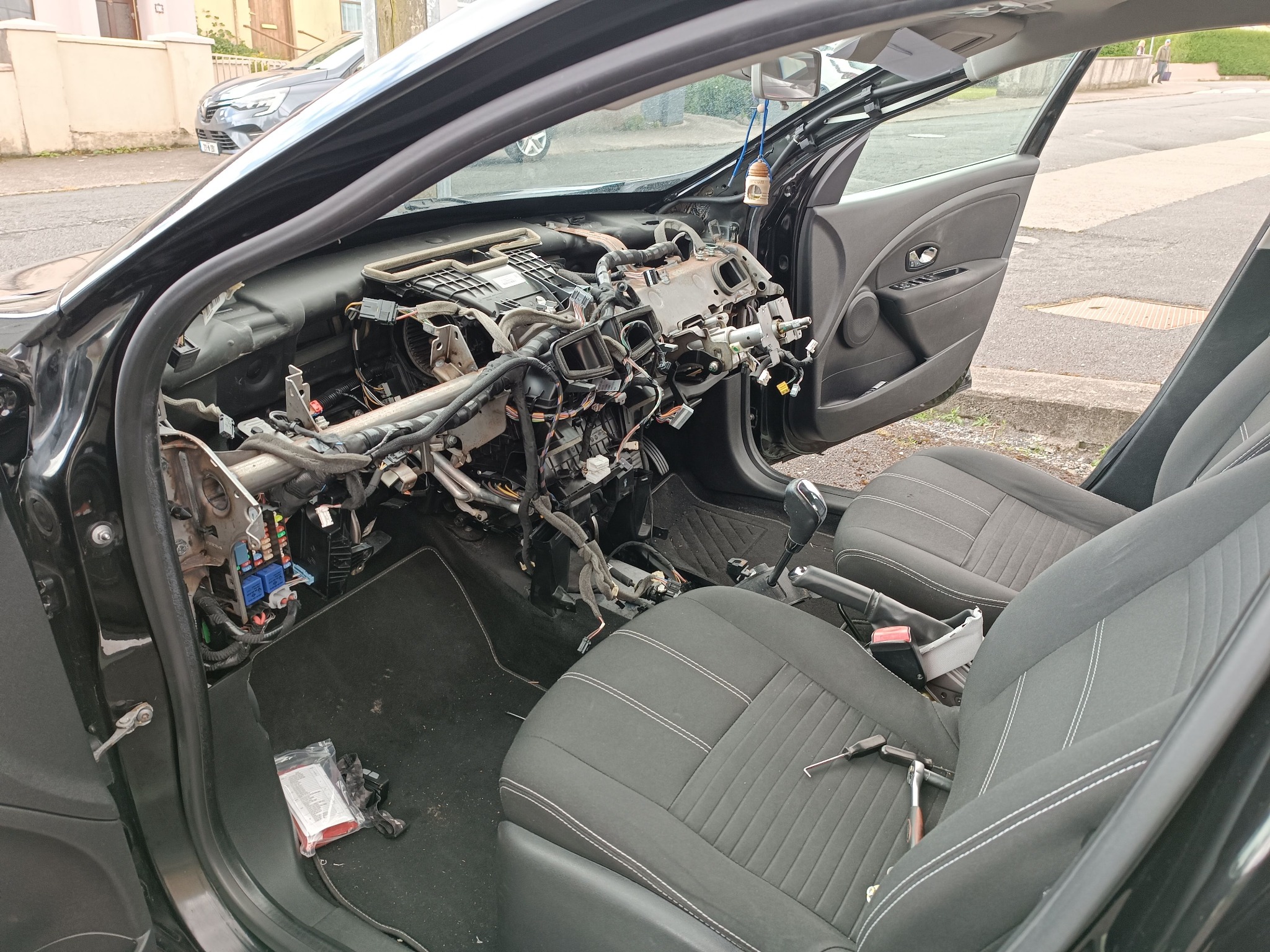 Wnętrze czarnego samochodu z rozmontowaną deską rozdzielczą, widoczne kable i elementy instalacji elektrycznej. Na siedzeniach leżą narzędzia.