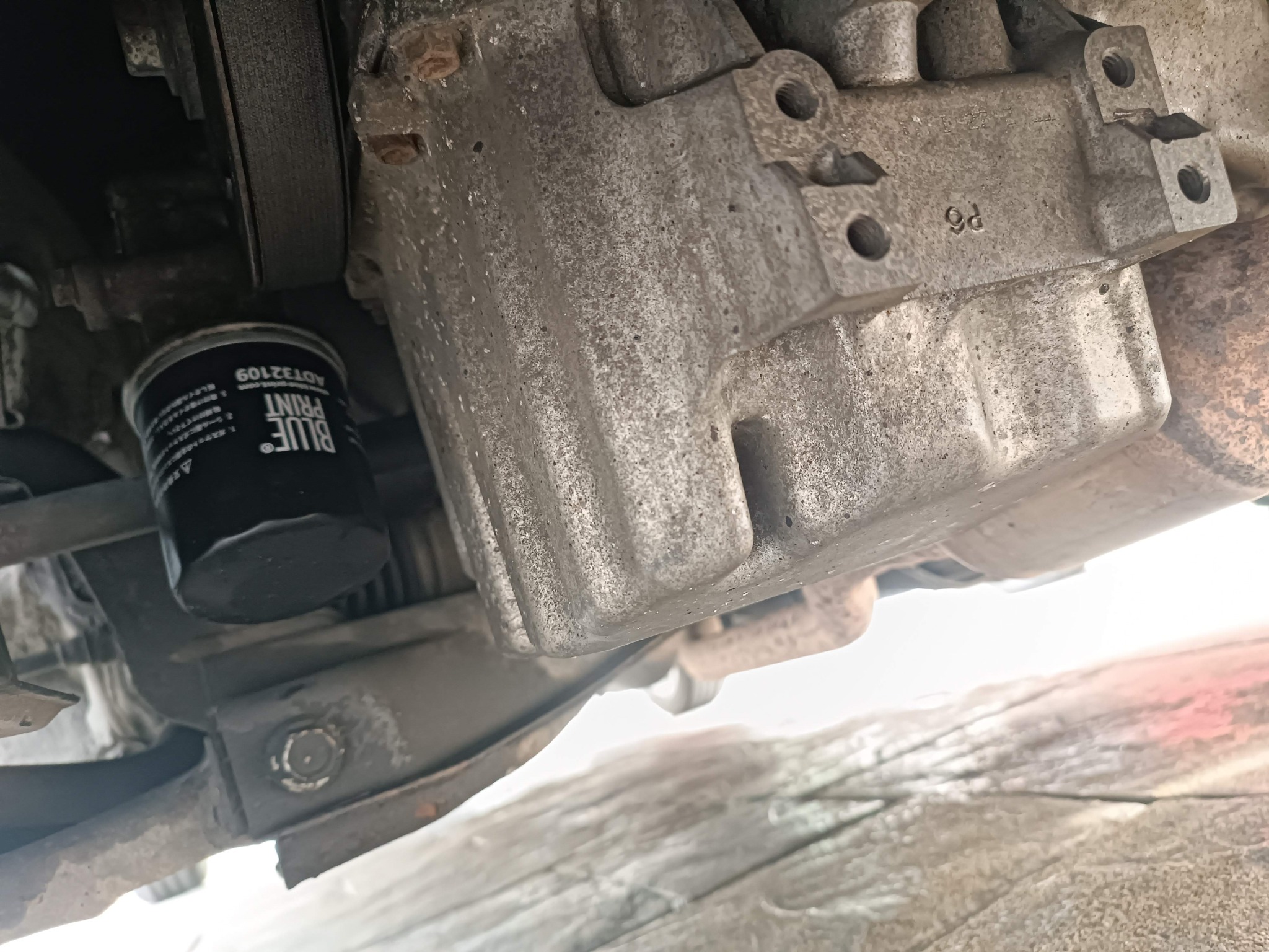 Widok od spodu na silnik samochodowy z nowym filtrem oleju marki Blue Print, ukazujący metalowe elementy zawieszenia i fragment układu wydechowego.