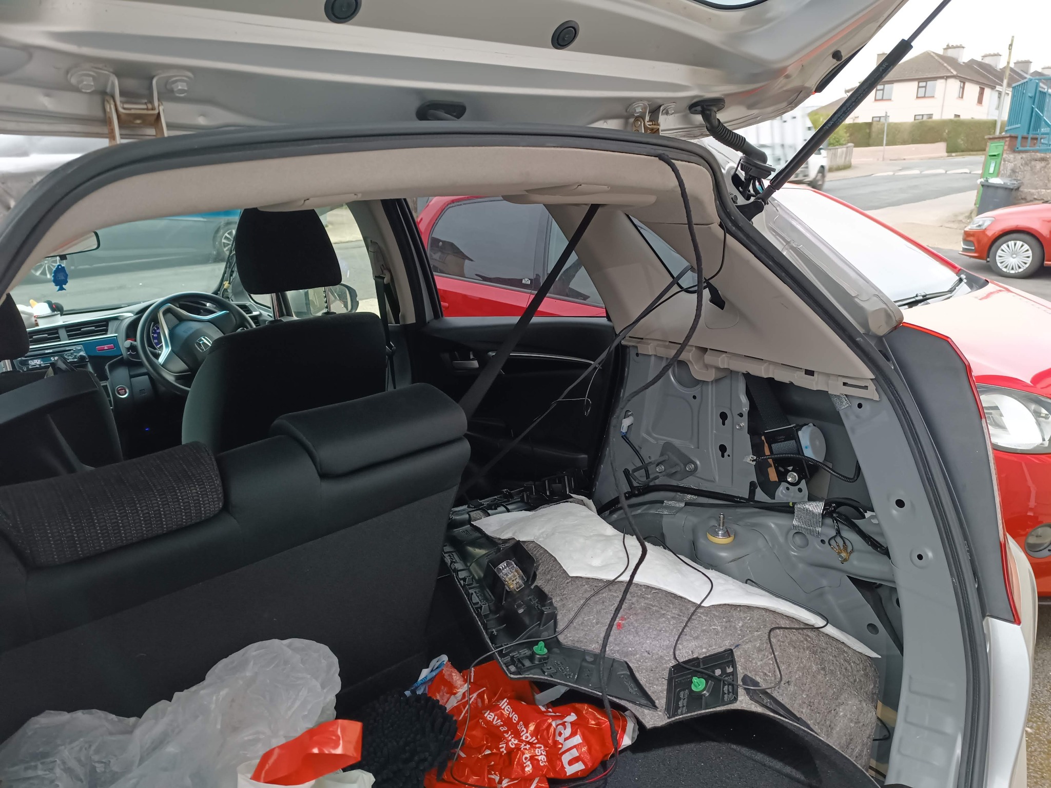 Wnętrze bagażnika samochodu w trakcie naprawy lub modyfikacji, z widocznymi elementami instalacji elektrycznej i demontażu tapicerki. Widoczne przewody i części.