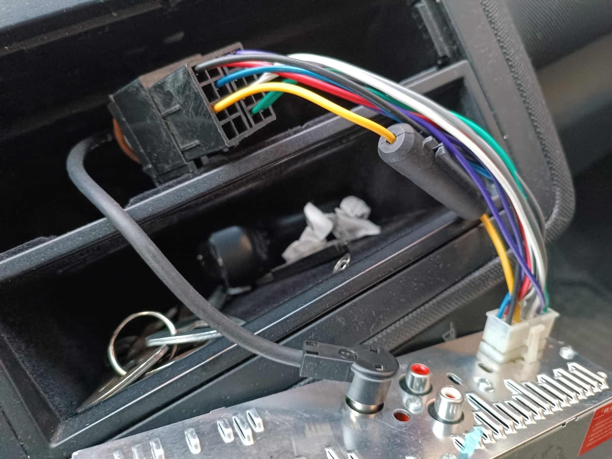 Podłączenie przewodów do panelu samochodowego audio. Widoczne kolorowe kable, złącza i fragment wnętrza pojazdu. Przewody wpięte do radia samochodowego.