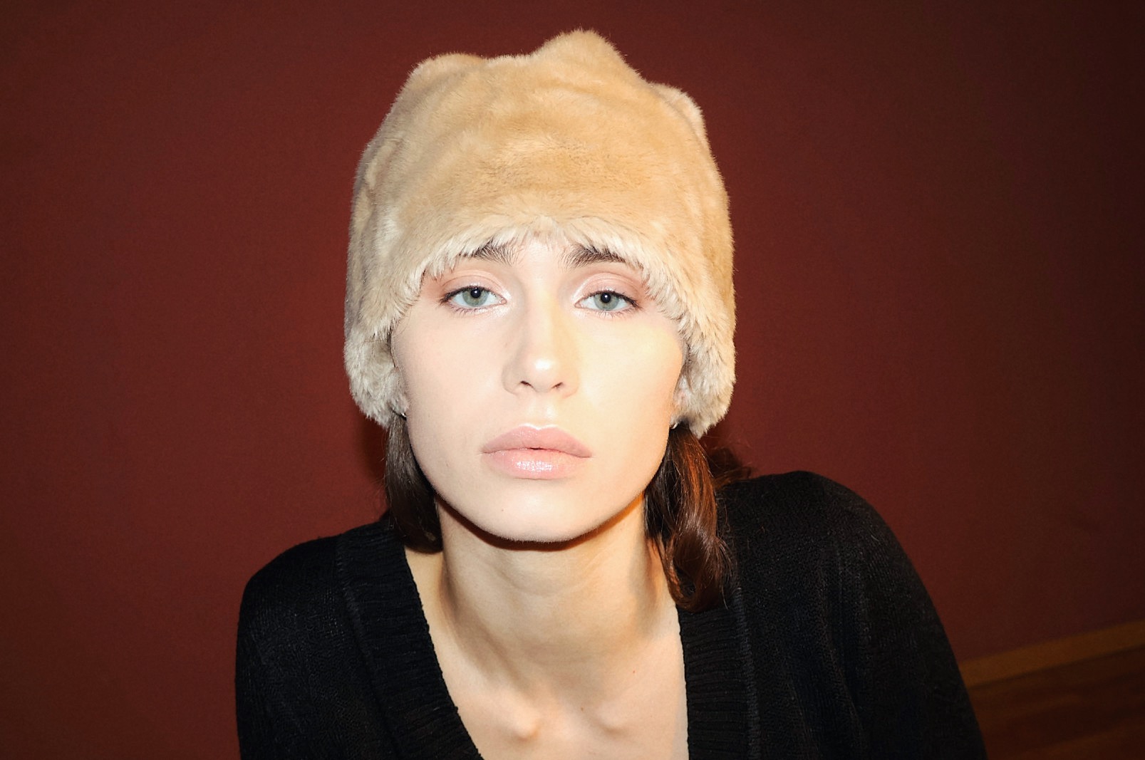 Portret kobiety w futrzanej czapce na tle bordowej ściany w Gdyni. Uwagę przyciągają jej jasne oczy i delikatny makijaż.