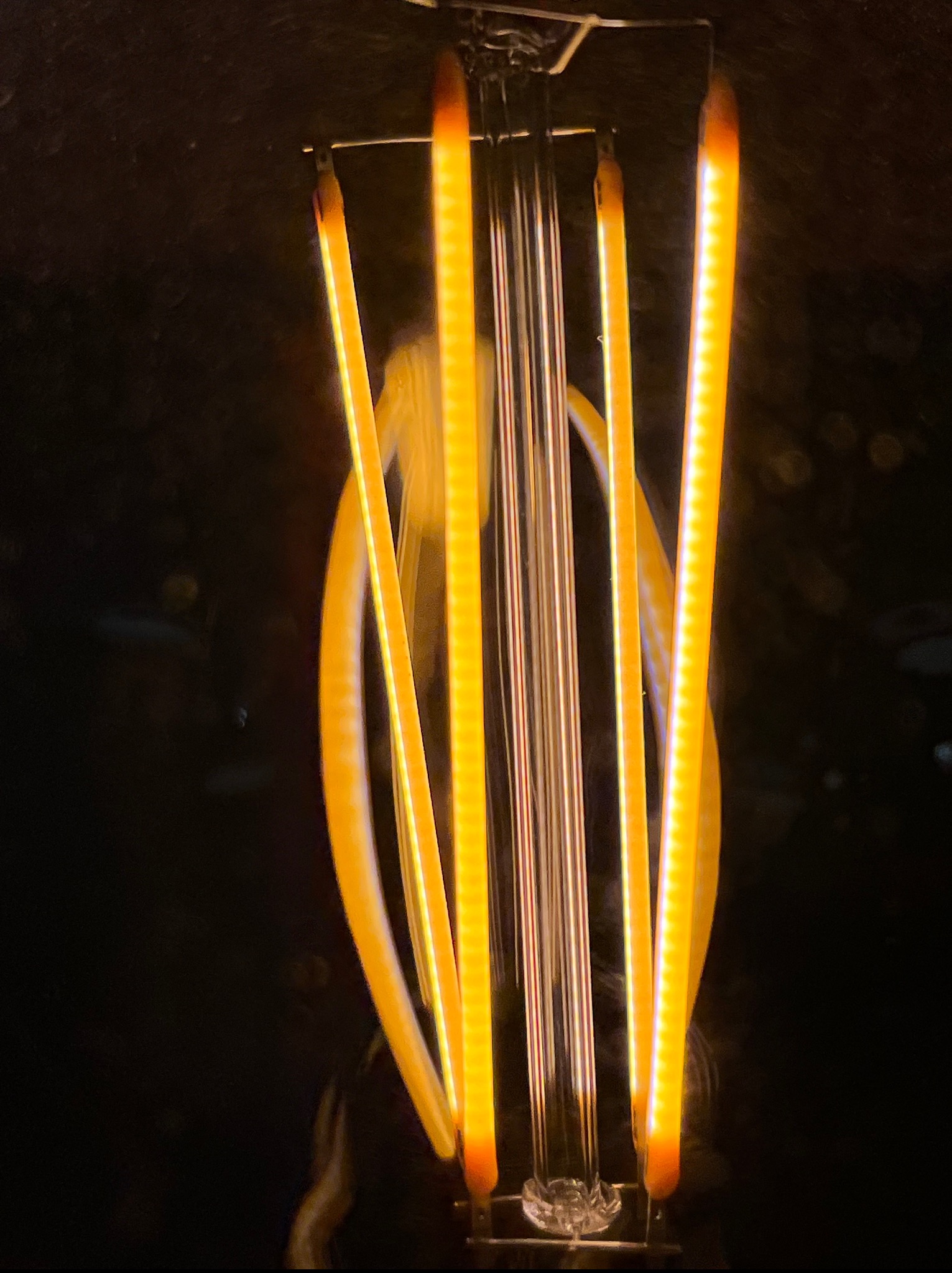 Detaliczne ujęcie żarówki LED z włóknami w ciepłym odcieniu, na ciemnym tle, ukazujące jej specyficzną budowę i emitowane światło. Minimalistyczny kadr.