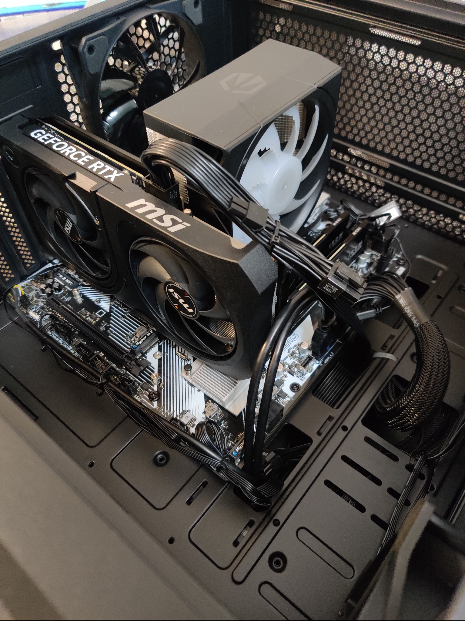 Wnętrze obudowy PC z kartą graficzną GeForce RTX MSI, chłodzeniem procesora z białym wentylatorem, płytą główną i uporządkowanym okablowaniem. Widok z góry.