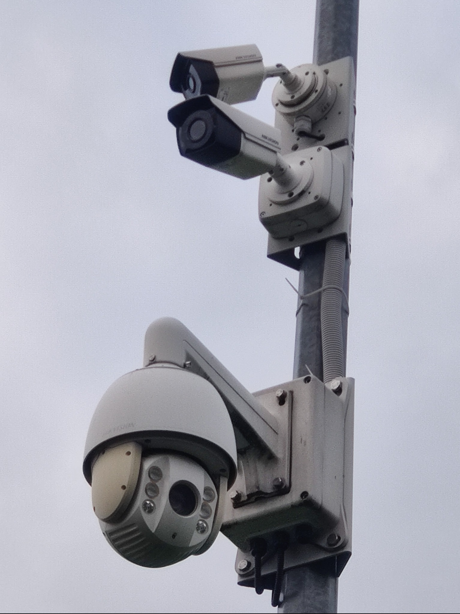 Zestaw kamer Hikvision na słupie w Ząbkach. Dwie kamery tubowe i jedna obrotowa, szare tło nieba. Widoczne elementy montażowe i przewody.