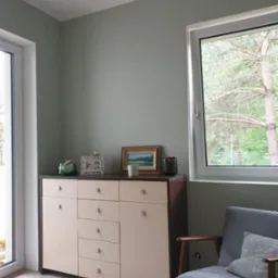 Pomalowane na szaro wnętrze pokoju z komodą, oknem z widokiem na drzewa i fotelem w stylu retro. Ściany gładkie, bez widocznych niedoskonałości.