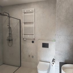 Custom Constructions - Nowoczesna łazienka z szarymi płytkami imitującymi beton, kabiną walk-in z czarną ramą, podwieszaną toaletą, białym grzejnikiem drabinkowym i umywalką z ryflowaną misą.