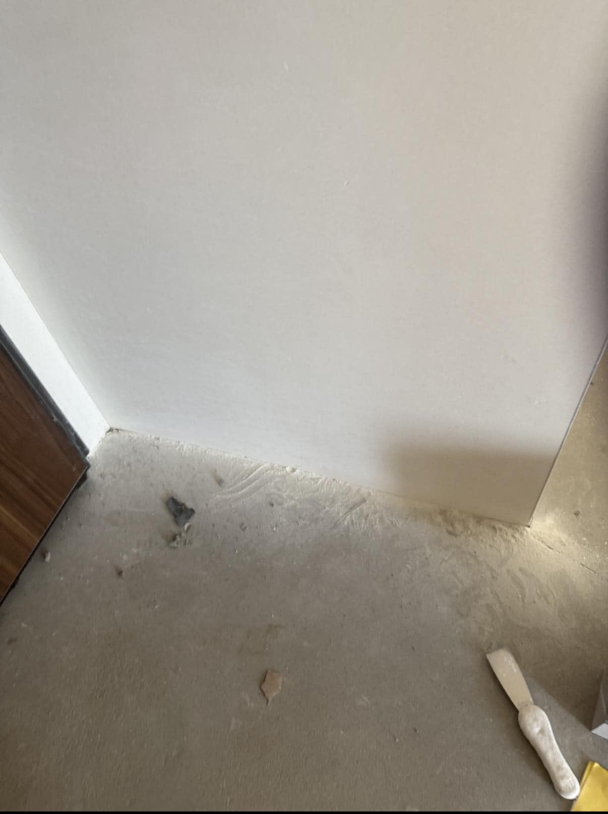 Świeżo wykończona ściana po remoncie, widoczny fragment podłogi z resztkami gładzi i narzędzie - szpachelka. Ujęcie z dołu, blisko ściany.