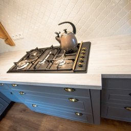 KAPI Szwarckopf - Meble Na Wymiar - Szare szafki kuchenne z blatem imitującym drewno, płyta gazowa SMEG i czajnik na tle białych płytek w marokańskim stylu. Ujęcie z dołu, podkreślające detale.