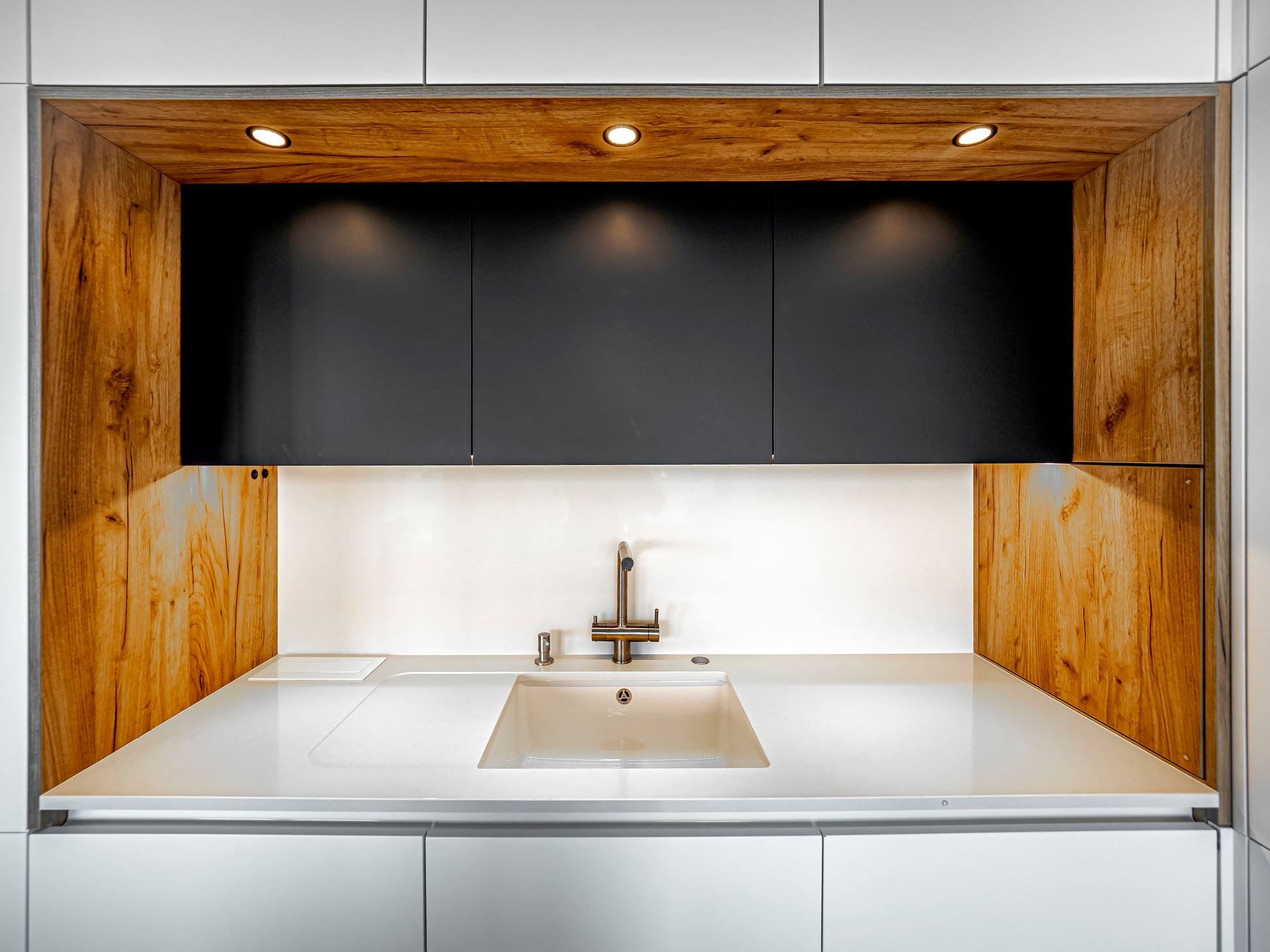 Nowoczesna kuchnia: Białe szafki dolne, drewniane boki i czarne szafki wiszące z oświetleniem punktowym nad białym zlewem ze stali nierdzewnej.