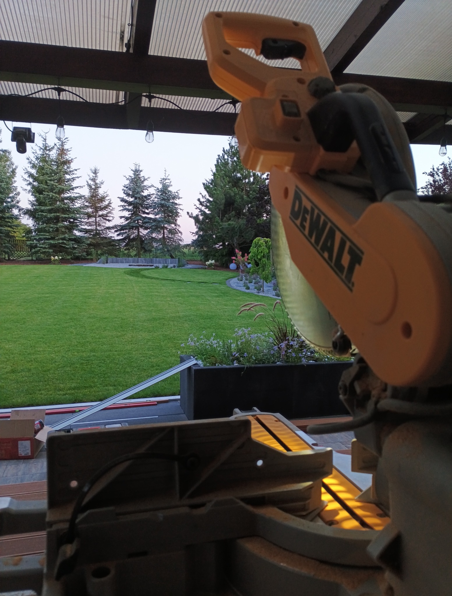 Ukośnica DeWalt na tarasie z widokiem na trawnik i drzewa. Przygotowania do układania paneli podłogowych na zewnątrz.