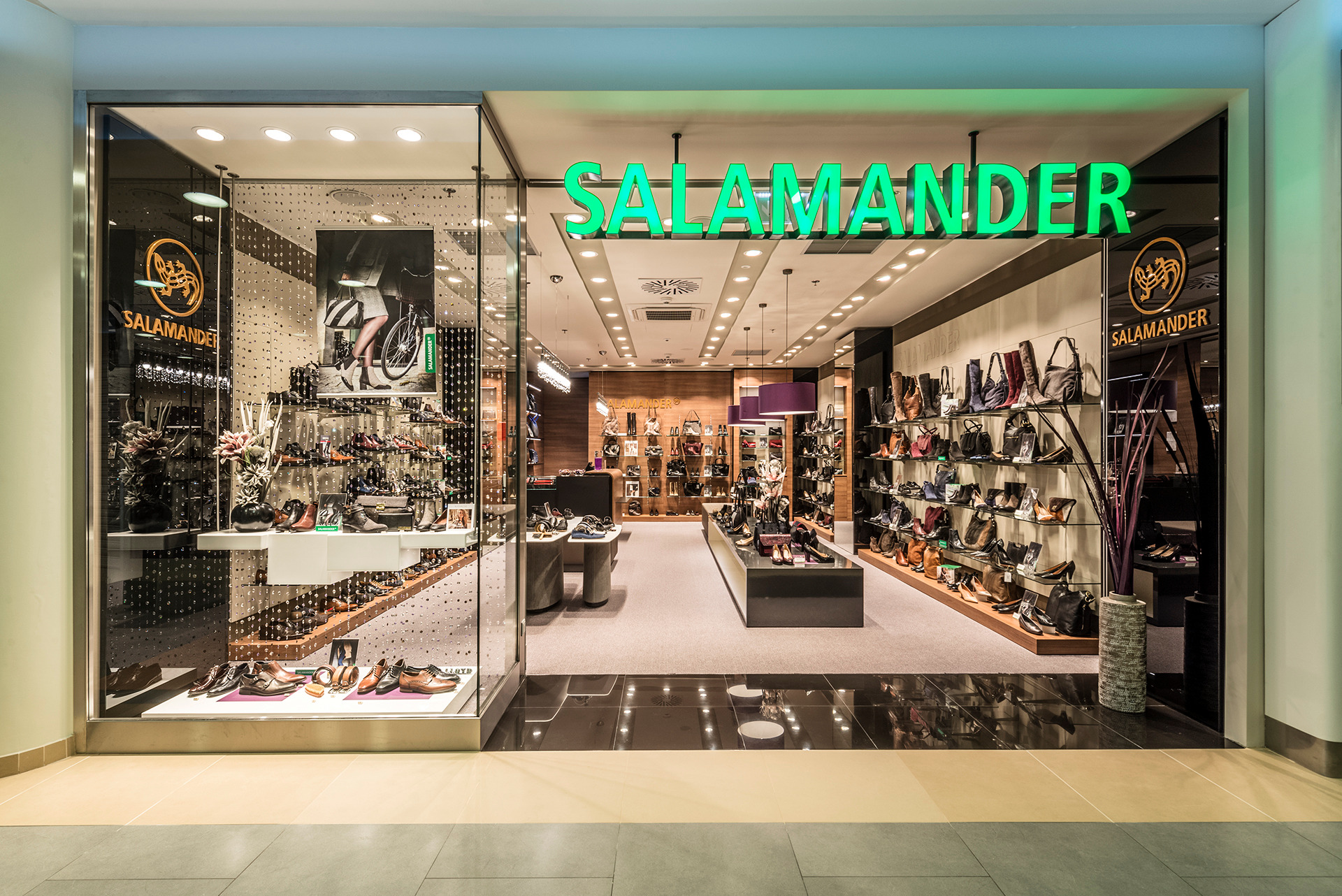 Elegancki butik Salamander z przeszkloną witryną, prezentujący kolekcję obuwia i torebek. Jasne wnętrze z oświetleniem punktowym, zielony neonowy szyld.