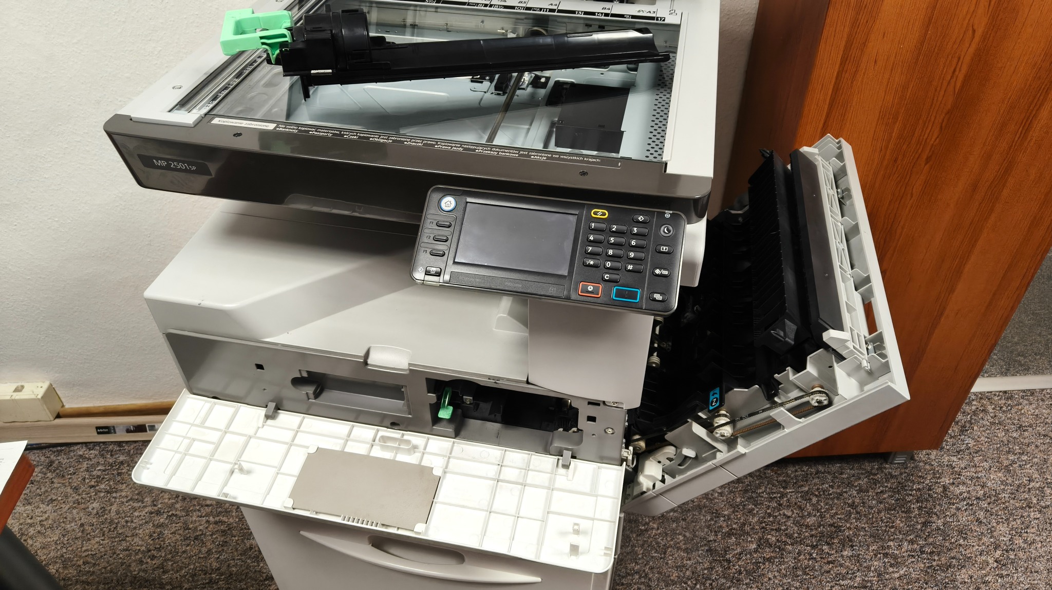 Uszkodzona kserokopiarka MP 2501SP z otwartymi panelami, widoczne wnętrze urządzenia. Serwis sprzętu biurowego w Płocku. Nietypowy kąt ujęcia.