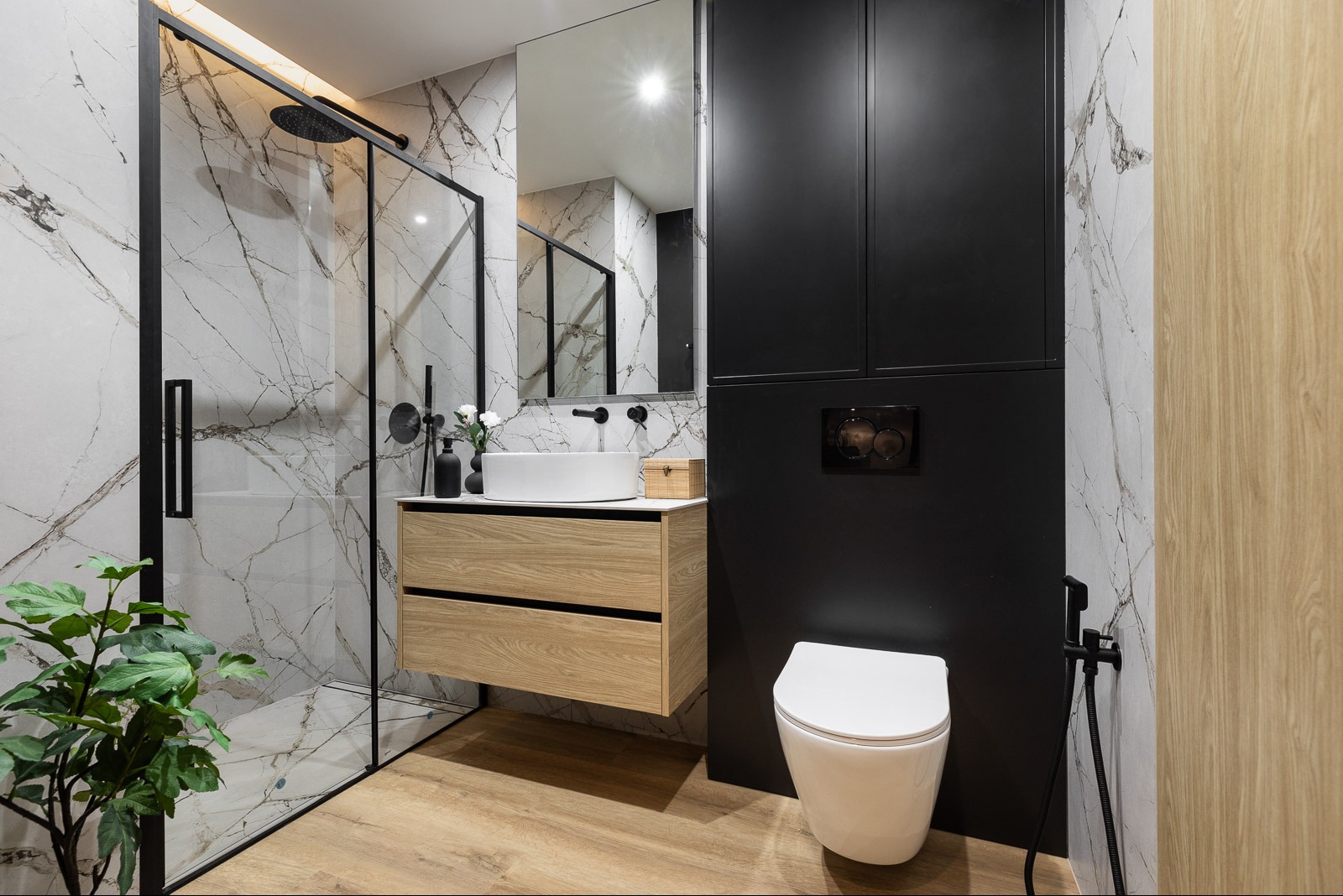 Nowoczesna łazienka z kabiną prysznicową typu walk-in, umywalką nablatową na drewnianej szafce, czarnymi elementami armatury i marmurowymi płytkami ściennymi.