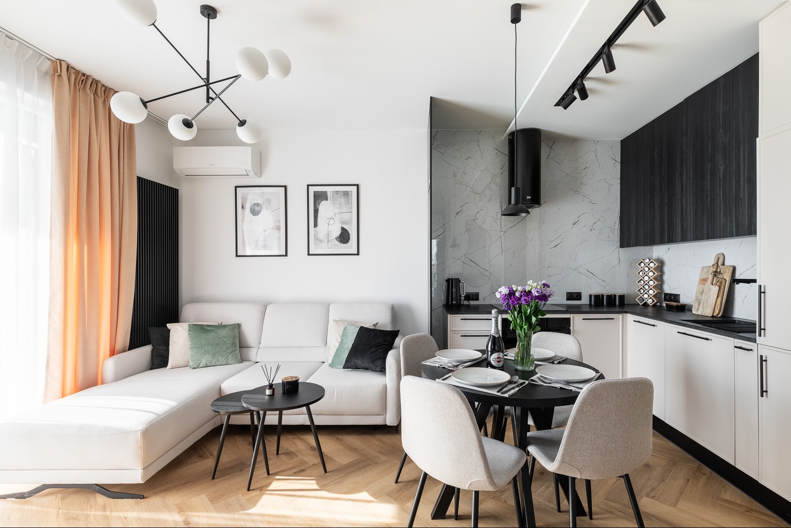 Jasne wnętrze mieszkania po remoncie: salon z sofą, jadalnia ze stołem i kuchnia z marmurowym blatem. Nowoczesne oświetlenie i drewniana podłoga.