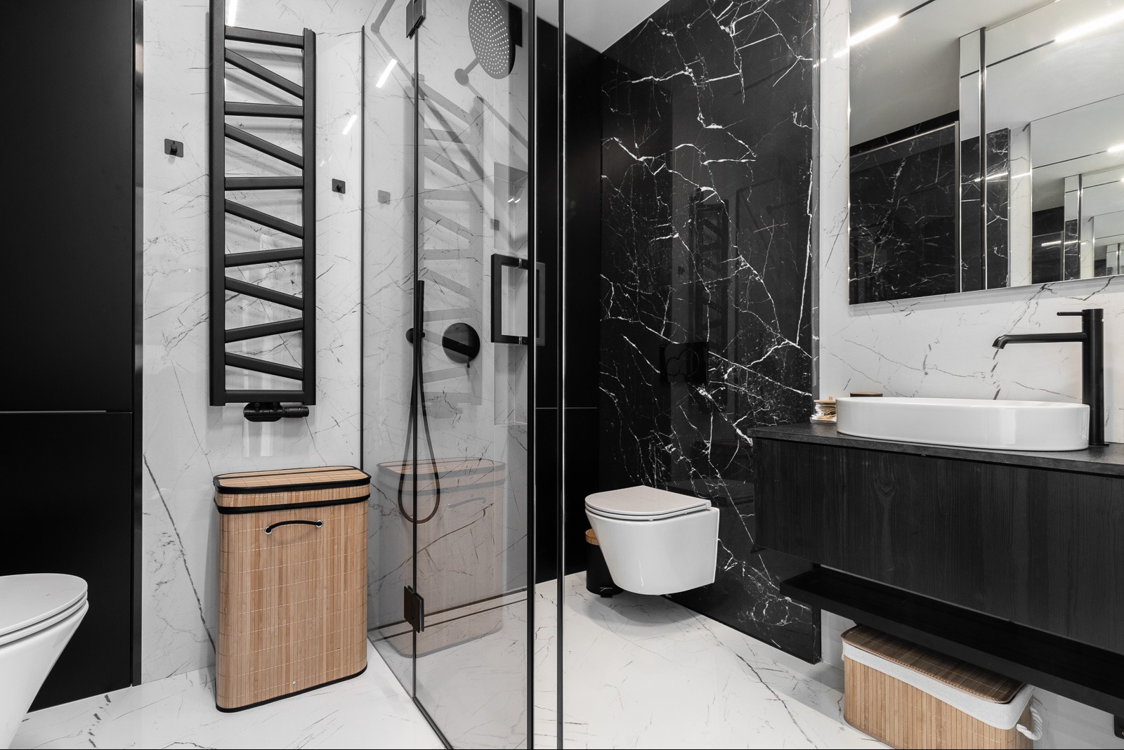 Nowoczesna łazienka z czarnym marmurem, kabiną prysznicową ze szkła i bambusowym koszem na pranie. Minimalistyczny design z czarną armaturą i białymi elementami.