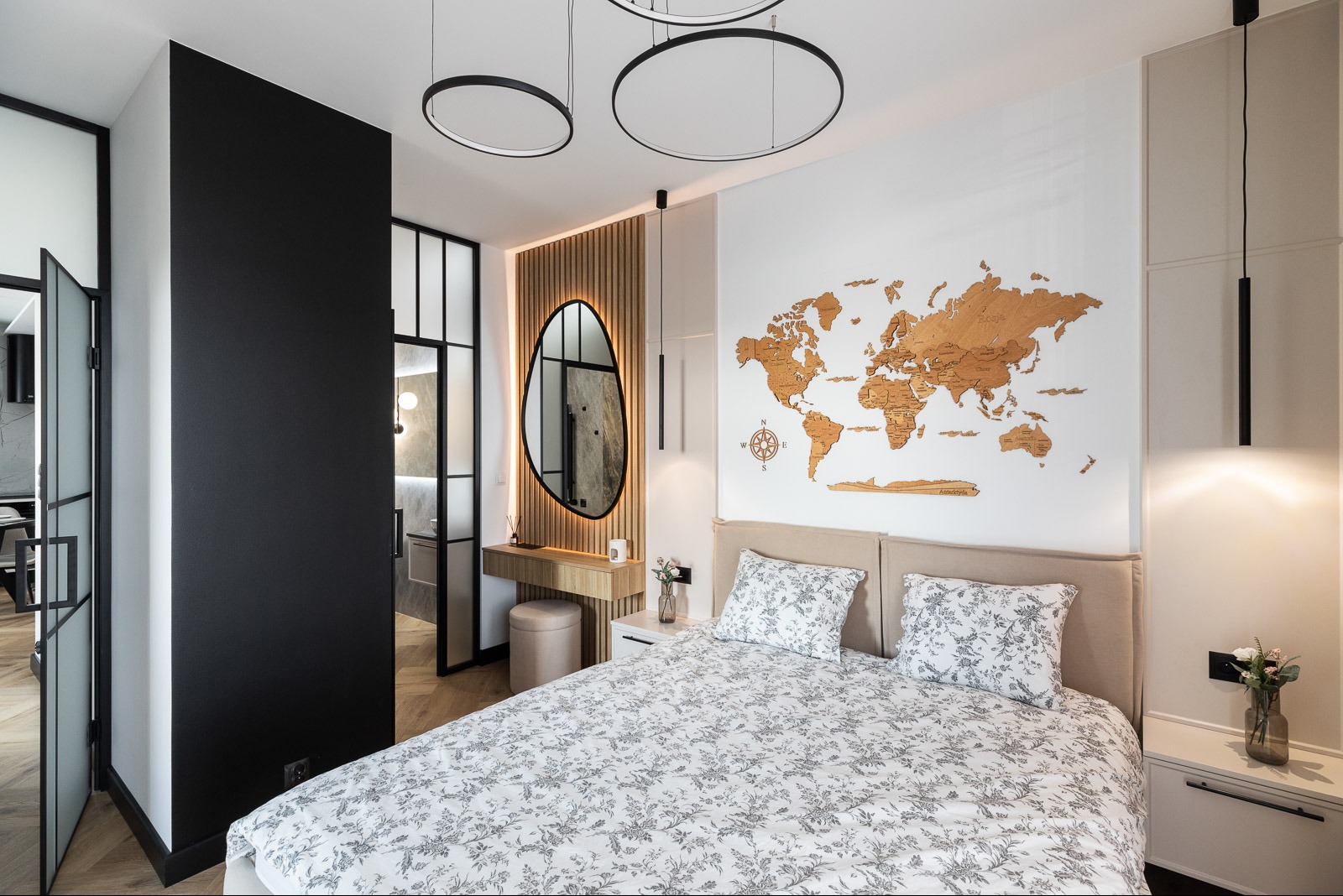 Nowoczesna sypialnia z drewnianą mapą świata na ścianie, owalnym lustrem z podświetleniem i czarnymi, minimalistycznymi lampami wiszącymi.