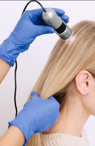 Trichoskopia włosów blond, badanie skóry głowy z bliska przy użyciu urządzenia diagnostycznego przez specjalistę w niebieskich rękawiczkach.