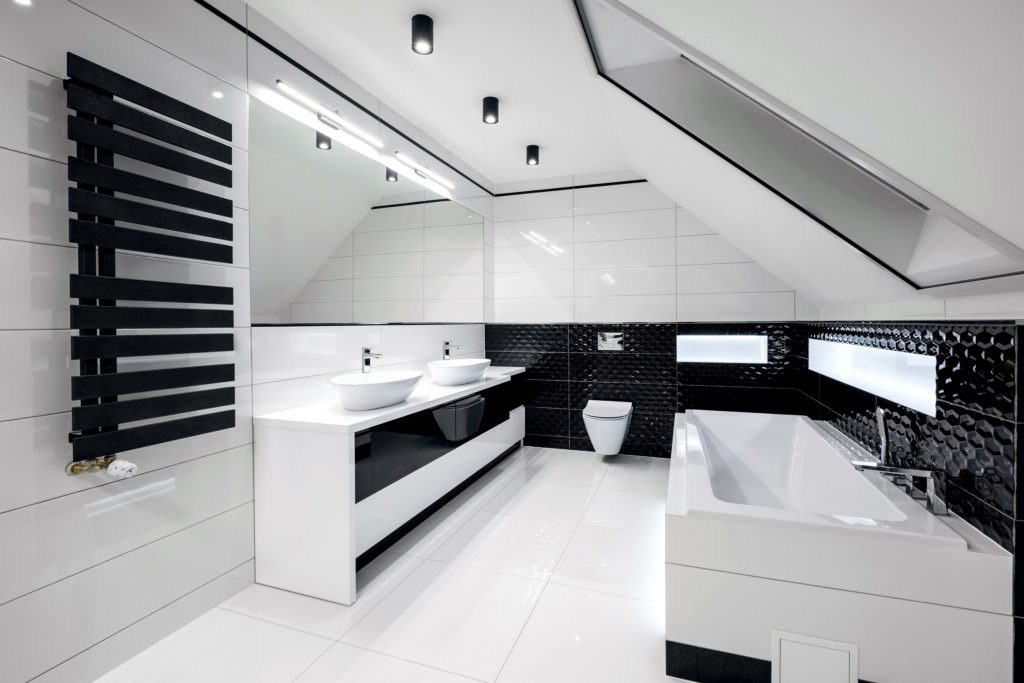 Elegancka, czarno-biała łazienka na poddaszu z umywalkami nablatowymi, grzejnikiem drabinkowym i wanną obudowaną płytkami. Nowoczesne oświetlenie sufitowe.