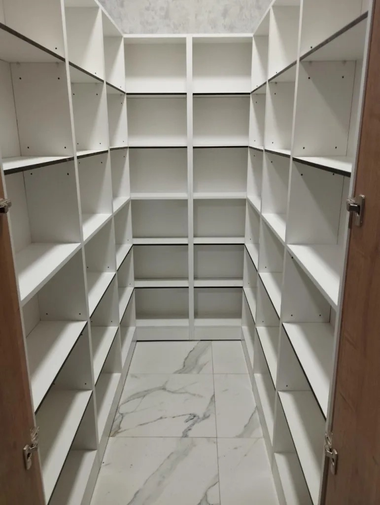 Biała, zabudowana garderoba z półkami, widok z otwartych drzwi. Marmurowe płytki na podłodze. Realizacja w Żorach.