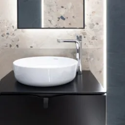 Nowoczesna łazienka: biała umywalka nablatowa na czarnej szafce, chromowana bateria, lustro z podświetleniem LED, ściany z płytek imitujących kamień.