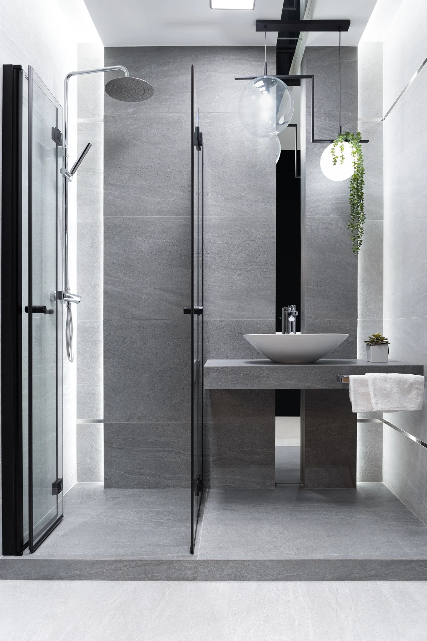 Nowoczesna łazienka w szarościach: kabina prysznicowa z czarnymi ramami, umywalka nablatowa na betonowym blacie, designerskie lampy wiszące i minimalistyczny wystrój.