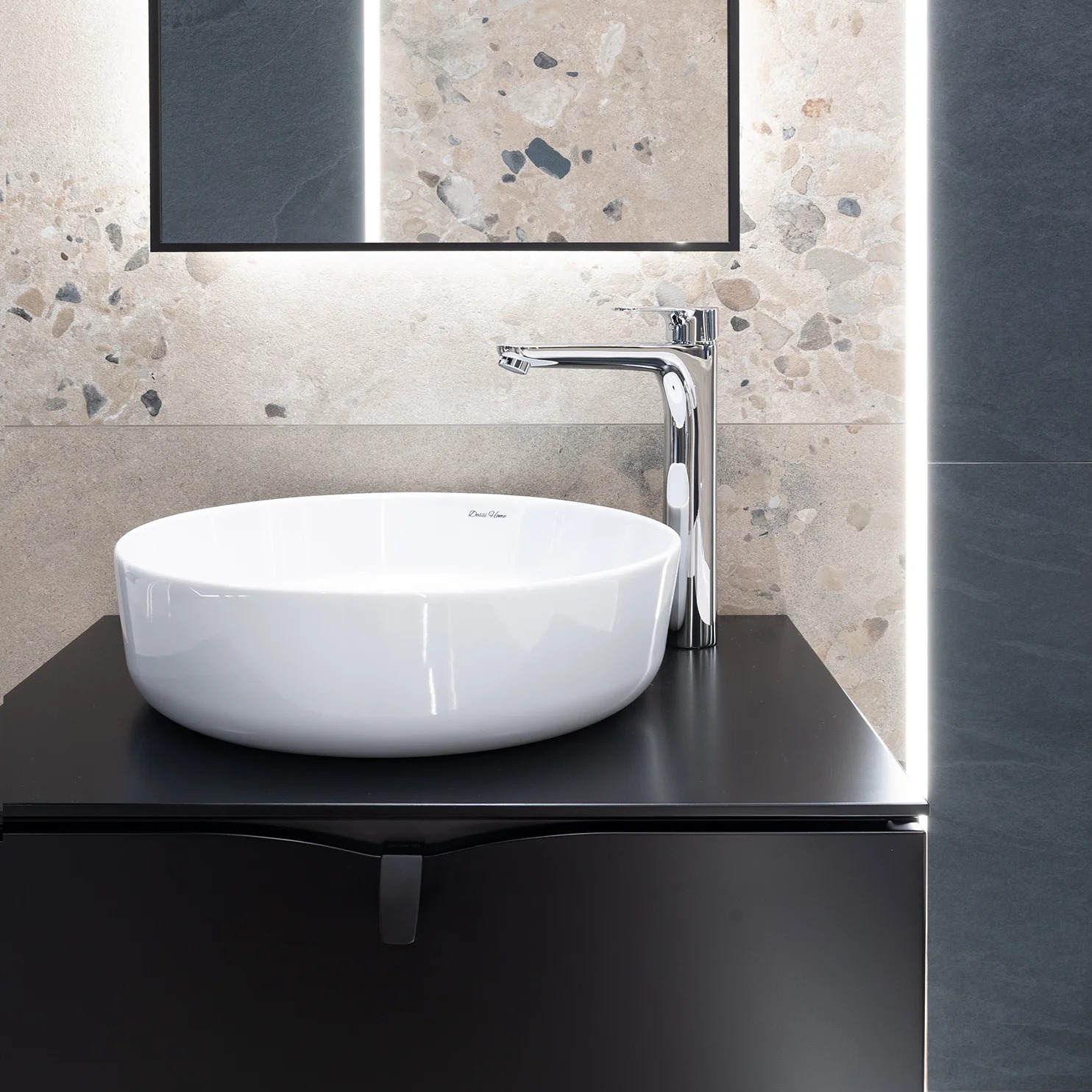 Nowoczesna łazienka: biała umywalka nablatowa na czarnej szafce, chromowana bateria, lustro z podświetleniem LED, ściany z płytek imitujących kamień.