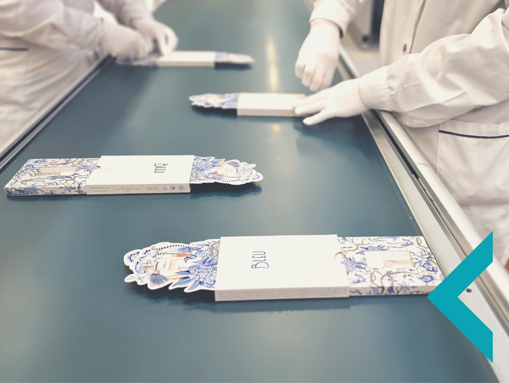 Pracownicy w białych uniformach pakują ozdobne pudełka z motywem niebieskich kwiatów na linii produkcyjnej. Widok z perspektywy.