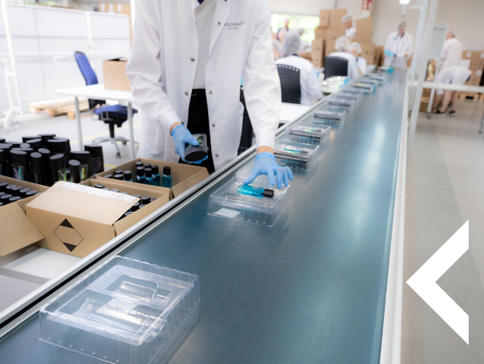 Pracownik w Józefowie umieszcza kosmetyki w plastikowych opakowaniach na linii produkcyjnej. Jasne, sterylne otoczenie, precyzja w pakowaniu produktów.