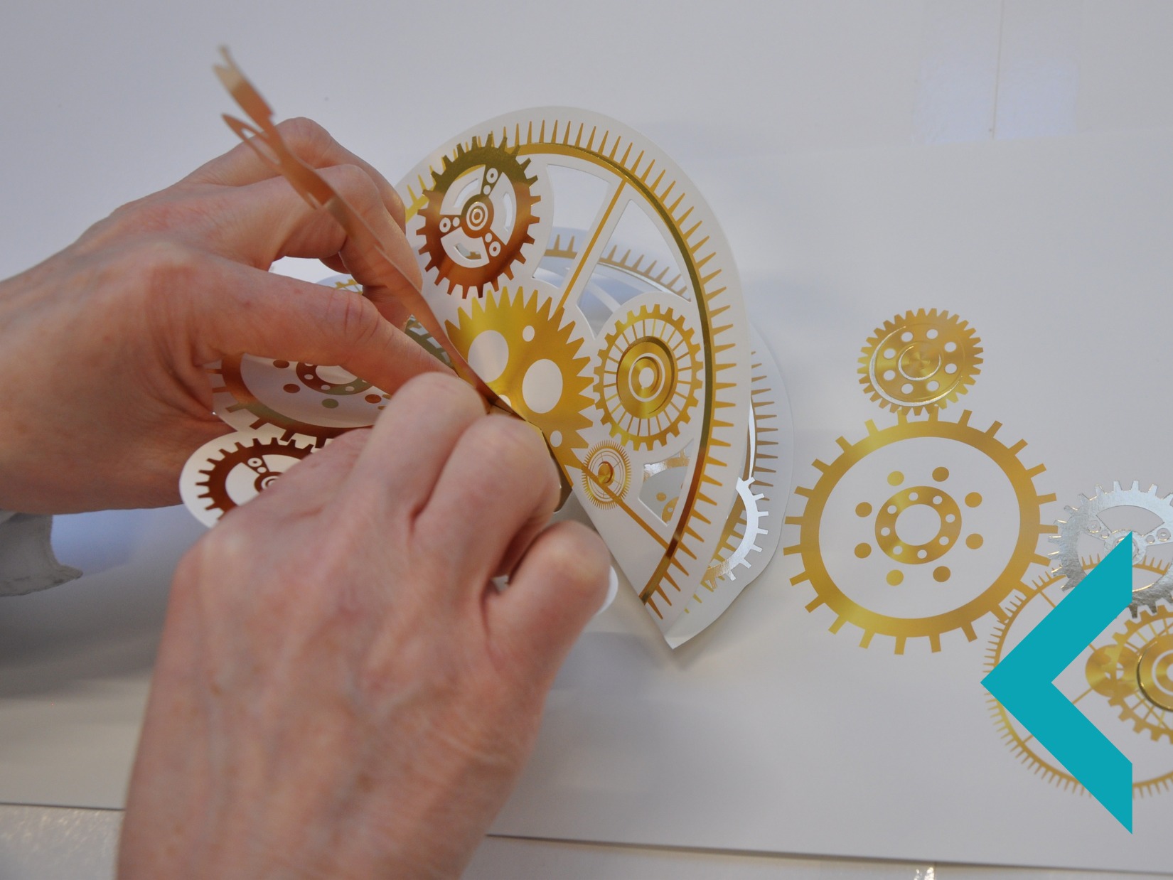 Naklejki z motywem złotych i srebrnych zębatek naklejane na białą powierzchnię, precyzyjna aplikacja przez osobę. Dekoracyjny element.