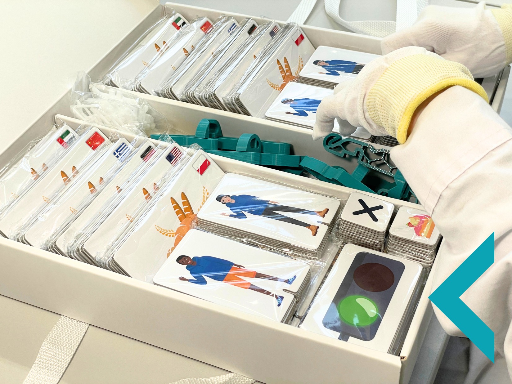 Ręczne pakowanie zestawu edukacyjnego: karty z flagami, postaciami i symbolami, umieszczone w białym pudełku z przegródkami i zielonymi elementami mocującymi.