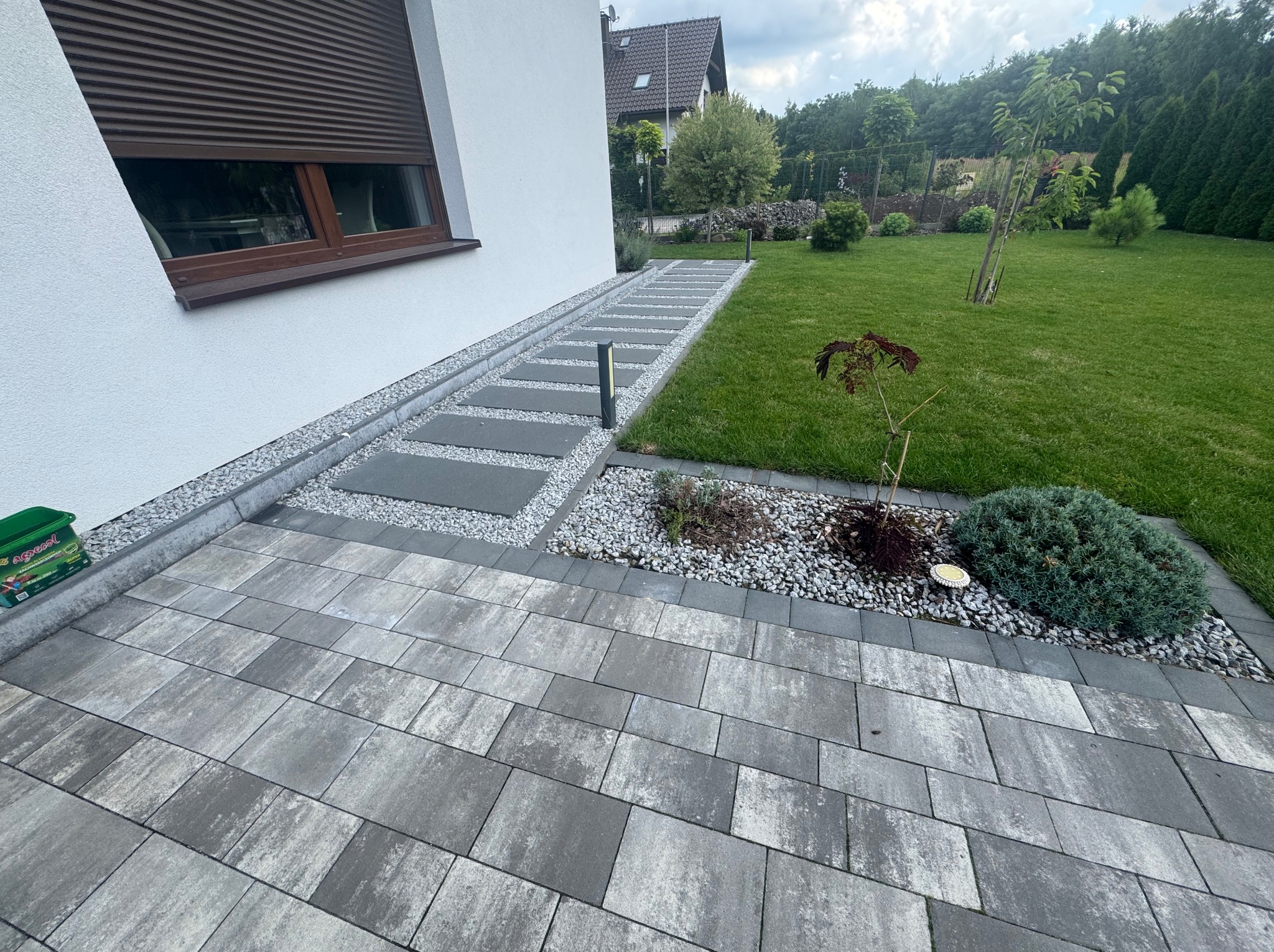 Ścieżka z płyt betonowych i kostki brukowej w ogrodzie, z widocznym trawnikiem i elementami małej architektury. Nowoczesny design z użyciem szarych odcieni.