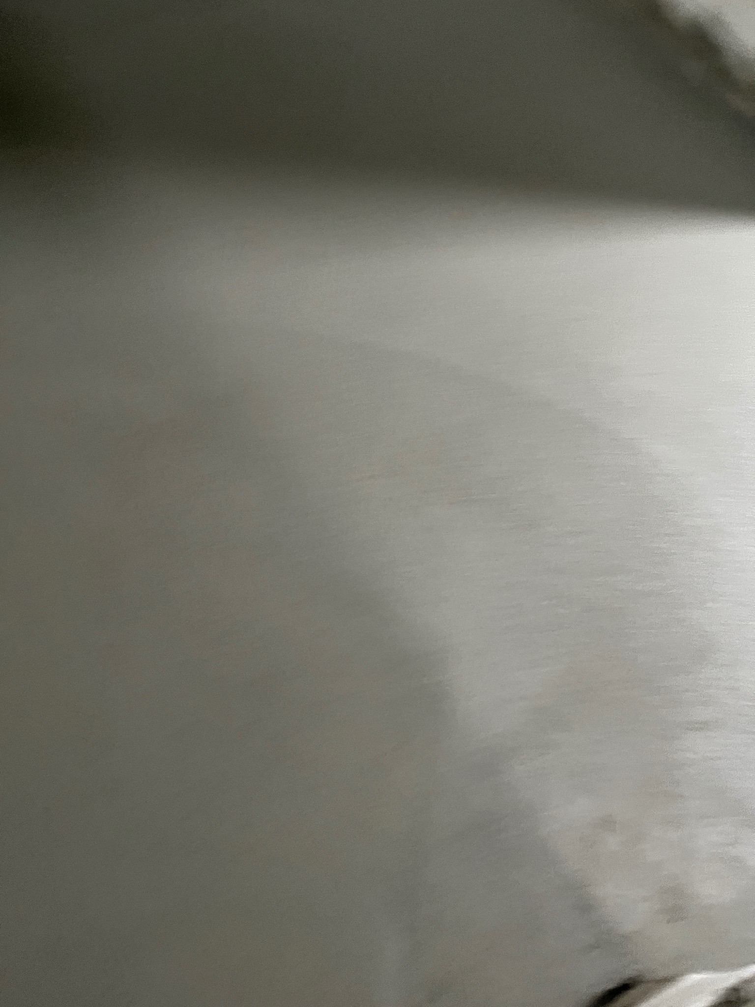 Gładka, szara powierzchnia, prawdopodobnie świeżo wylana posadzka. Widoczne delikatne smugi i refleksy światła. Minimalistyczny kadr, brak wyraźnych detali.