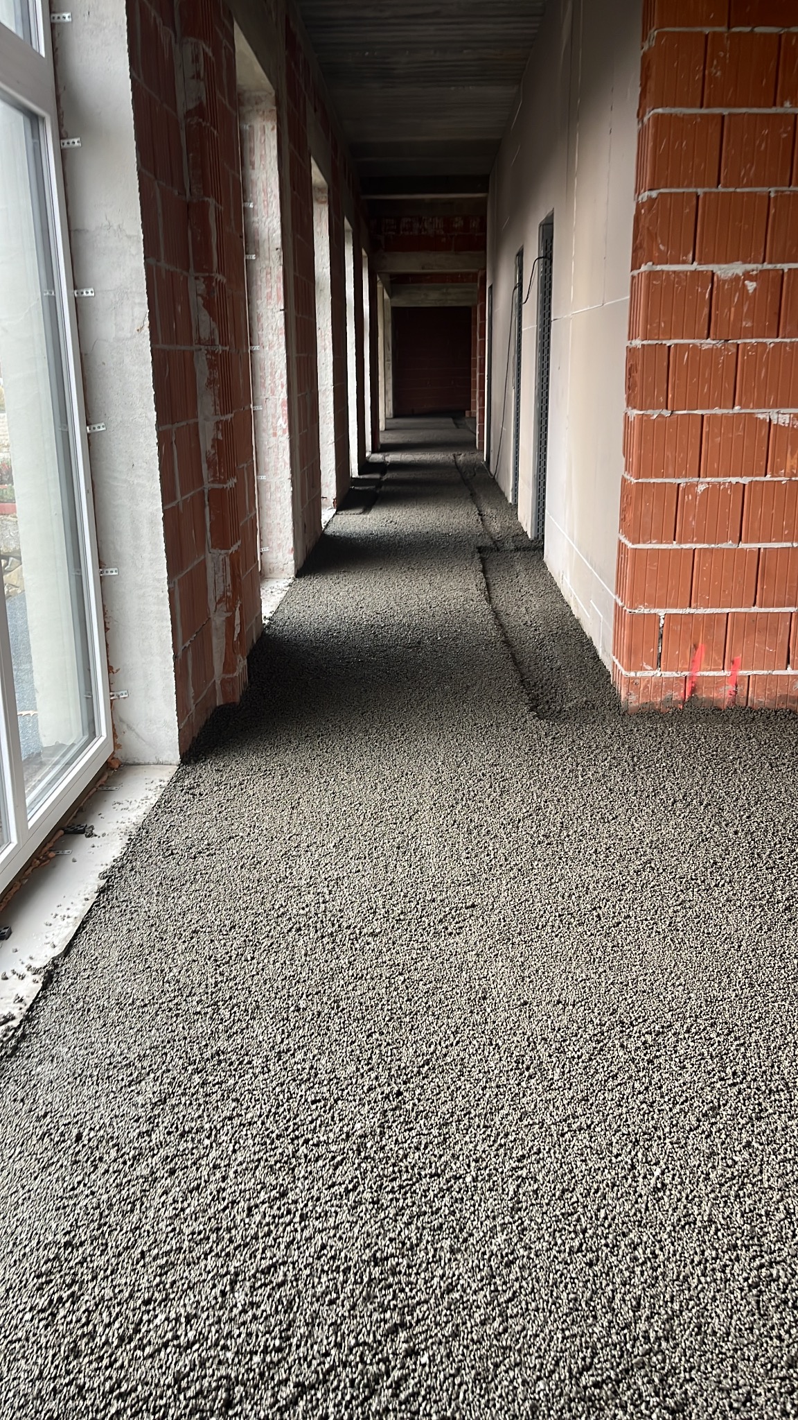 Wylewka jastrychowa w korytarzu budynku w Gromniku. Widoczne ściany z cegły i okna. Szara, chropowata powierzchnia posadzki.