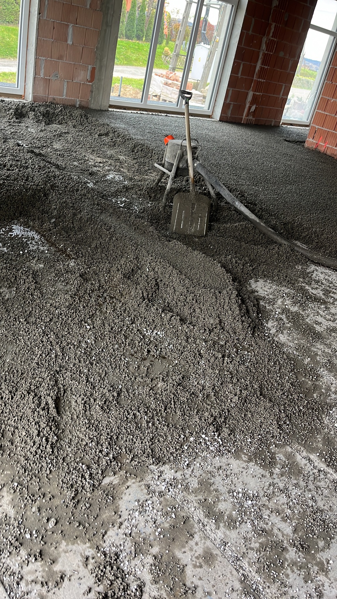 Wylewka jastrychowa w surowym wnętrzu z ceglanymi ścianami i dużymi oknami. Widoczna szpachla i maszyna do wylewania, co sugeruje etap prac w toku.