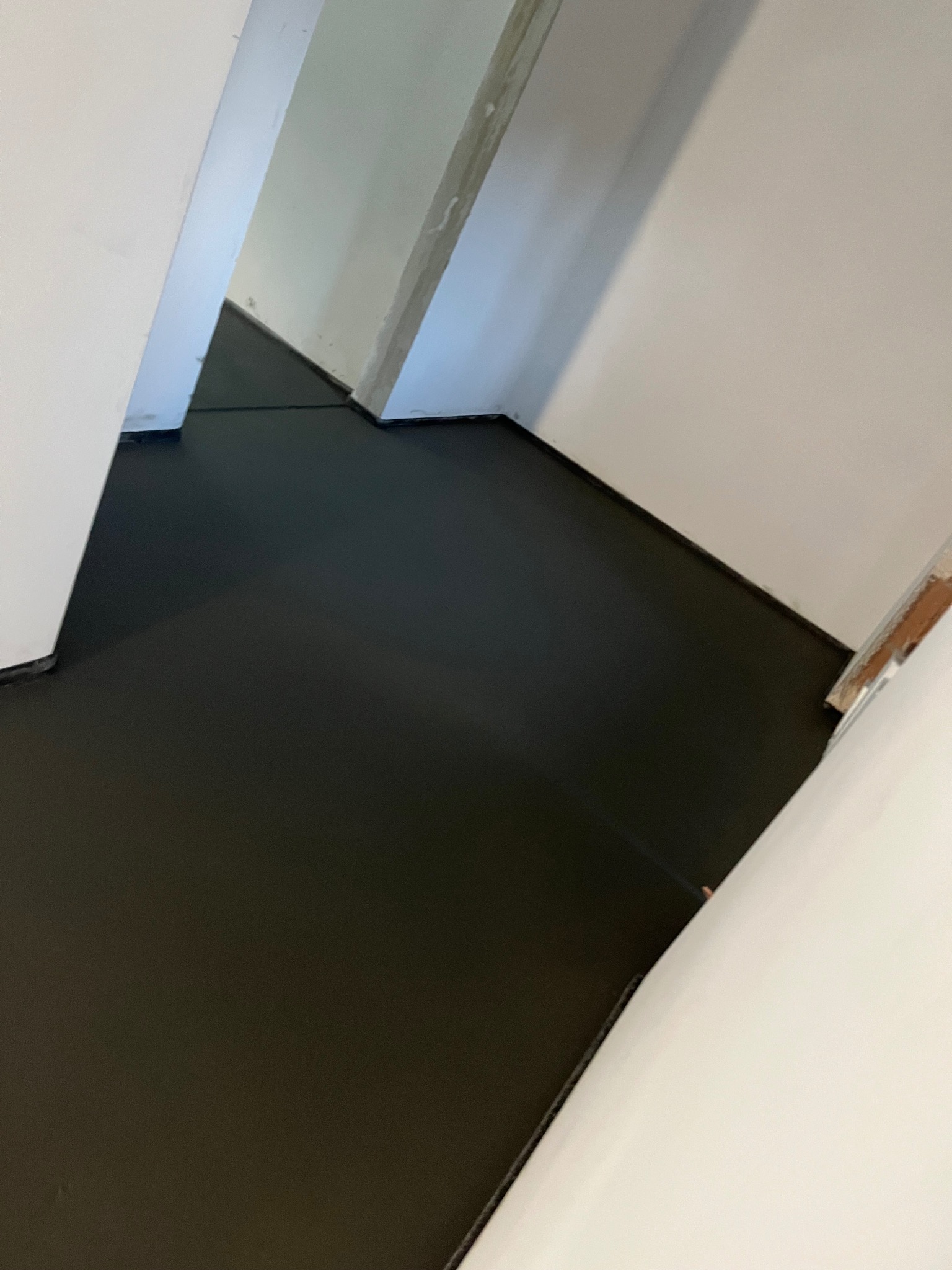 Minimalistyczne wnętrze z czarną, gładką posadzką mikrocementową, białe ściany i oświetlenie tworzą nowoczesny wygląd. Widok z góry podkreśla geometrię pomieszczenia.